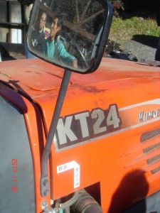 サイドミラーに金子さんの顔。トラクターの横に軽油と天ぷら油の表示は、冬は軽油で動かしてバイオジーゼルの天ぷら油を温めて利用する。